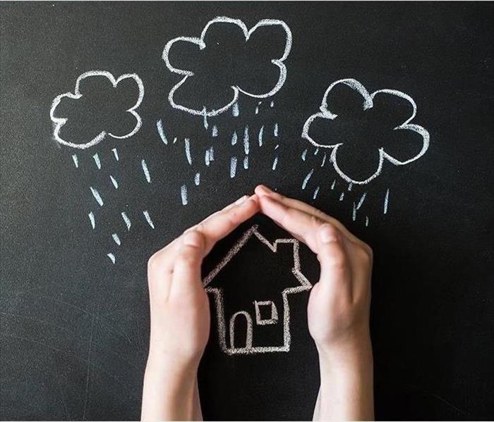 Chalkboard drawing of a house with rain clouds over it, and hands covering the house